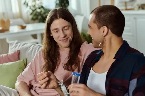 Ein schwules Paar, sitzt gemütlich auf einer Couch, genießt die Gesellschaft des anderen, zündet Marihuana in der gläsernen Bong an — Stockfoto