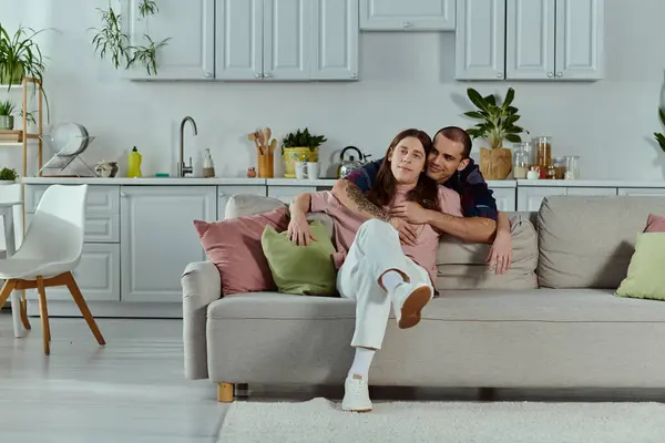 A gay couple in casual clothes relaxes on a couch in a cozy living room, smiling and enjoying each others company. — Stock Photo