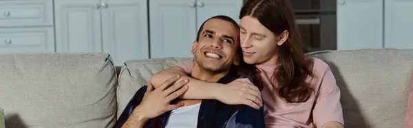 Гей-пару в повсякденному одязі обіймає один одного на зручному дивані вдома, розділяючи момент любові і любові. — стокове фото