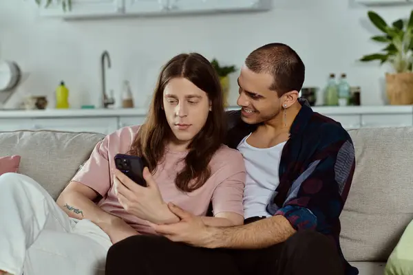 Same sex couple share a cozy moment on a couch, engrossed in a cell phone screen. — Stock Photo