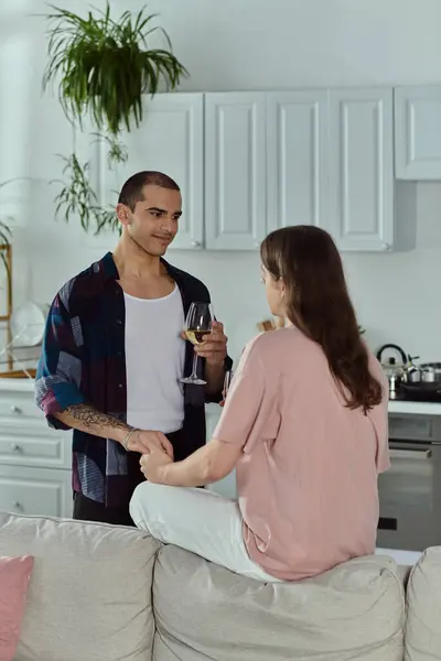A man in casual clothes holds a glass of wine while talking to a partner in a cozy home setting. — Stock Photo