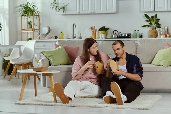A gay couple relaxes on a couch, enjoying a meal together at home, creating a cozy and intimate moment. — Stock Photo
