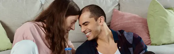 A gay couple, dressed casually, sits close together on a couch, holding glass bong — Stock Photo