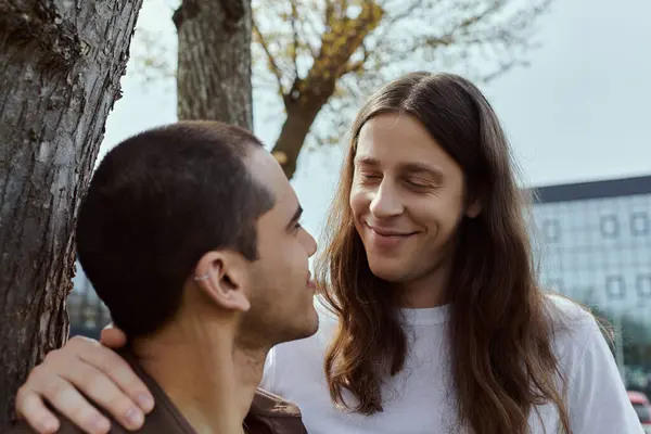 A gay couple in casual attire standing beside a tree, enjoying a peaceful moment outdoors together. — Stock Photo