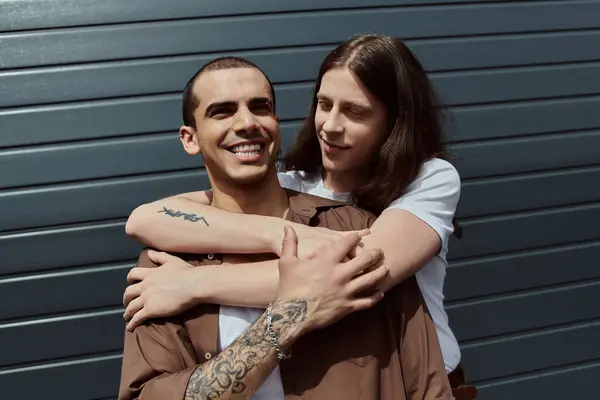 Un uomo abbraccia amorevolmente un partner con un tatuaggio sul braccio, mostrando tenero affetto in un ambiente esterno. — Foto stock