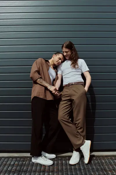 Dos hombres casualmente vestidos se paran uno al lado del otro, compartiendo un momento cerca de una puerta de garaje. - foto de stock