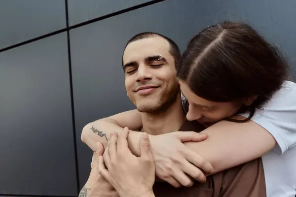 Una pareja gay, abrazar en un tierno abrazo durante un día al aire libre. - foto de stock