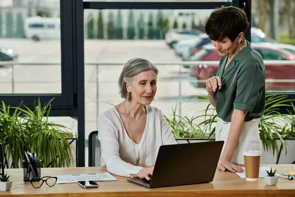 Two women sitting at a desk tackles tasks with her laptop. — Stock Photo