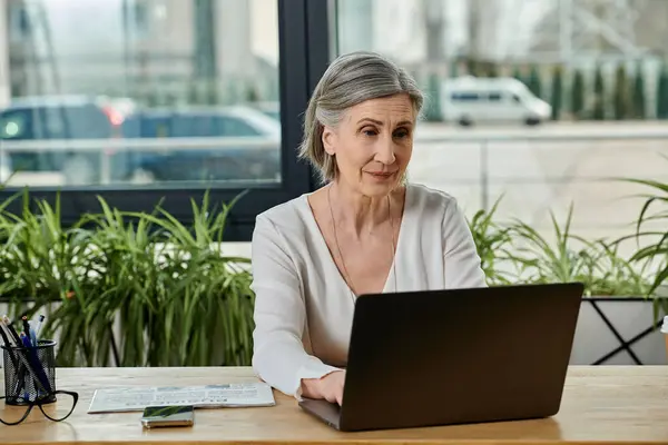 Uma mulher absorvida no trabalho em seu laptop em uma mesa. — Fotografia de Stock