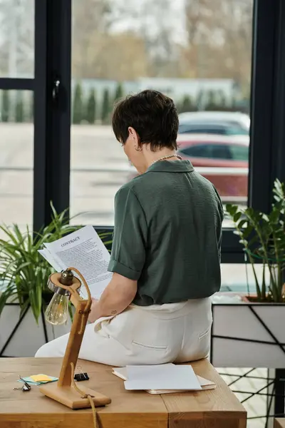 Mujer absorta en la lectura en su escritorio. - foto de stock