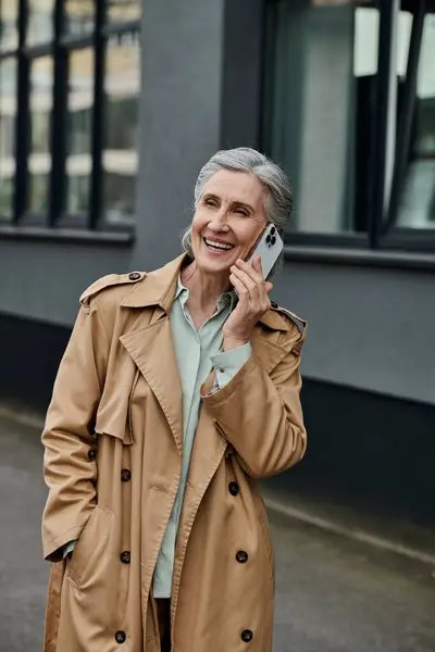Stylish woman in trench coat conversing on cell phone. — Stock Photo