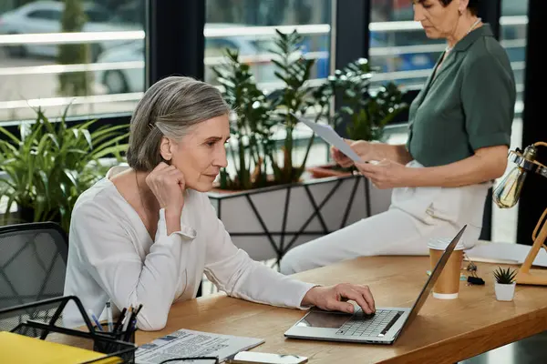 Zwei Frauen sitzen mit Laptop am Schreibtisch und arbeiten mit Papieren. — Stockfoto