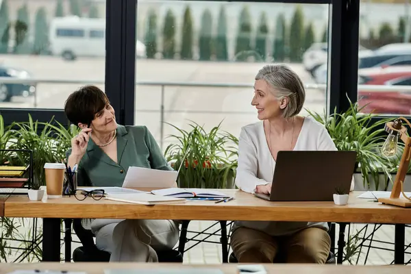 Two women work side by side on laptops in a modern office setting. — Stock Photo