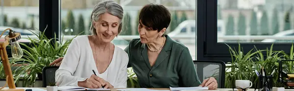 Two women working diligently at a desk with papers and pens. — Stock Photo