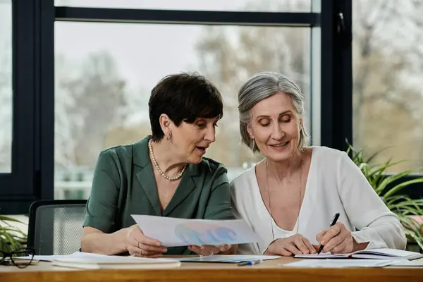Mature lesbian couple working together at a table, surrounded by papers. — Stock Photo