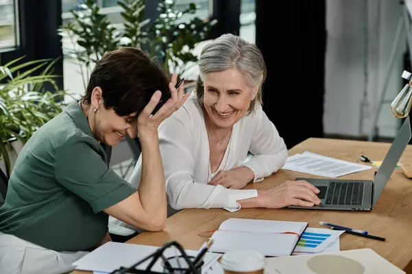 Two people, a mature, beautiful lesbian couple, sit at a table with a laptop, working together in an office setting. — Stock Photo