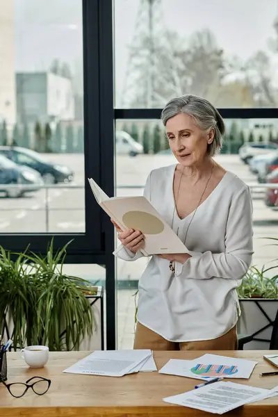 Una mujer lee pacíficamente un documento en su escritorio. - foto de stock