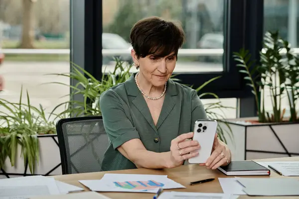 Mujer sentada en la mesa, sosteniendo el teléfono celular. - foto de stock