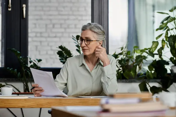A woman, sitting at a desk, holds a paper in her hand. — Stock Photo