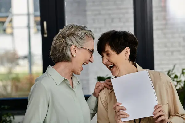 Two mature women, one with short hair and the other with long hair, stand side by side in an office setting. — Stock Photo