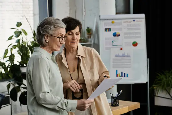 Two women pose by graphs and working together. — Stock Photo