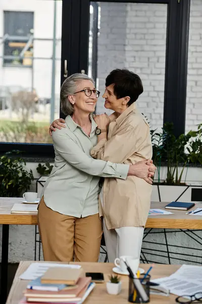 Una pareja de lesbianas maduras, de pie juntas, colaborando en un entorno de oficina. - foto de stock