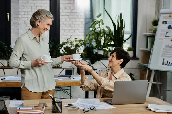 A woman passes a cup of coffee to another woman in an office setting. — Stock Photo