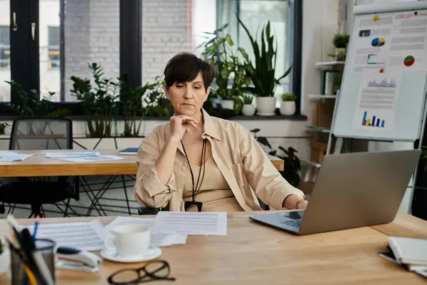 Eine reife Frau arbeitet an ihrem Laptop an einem Tisch im Büro. — Stockfoto