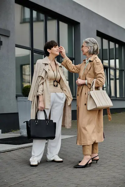Two women, a mature and beautiful lesbian couple, standing together in front of a building. — Stock Photo