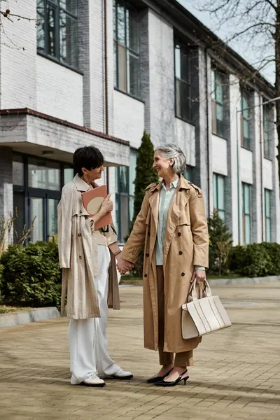 Two women, a mature beautiful lesbian couple, standing hand in hand in front of a building. — Stock Photo