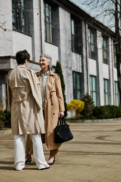 Um casal lésbico maduro e bonito de pé elegantemente na frente de um grande edifício. — Fotografia de Stock