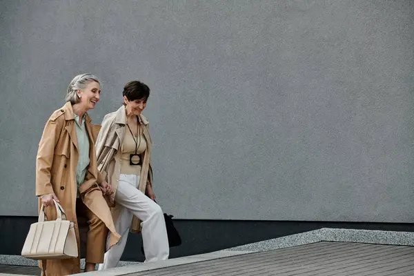 Due donne mature che trasportano borse, camminando lungo il marciapiede occupato della città. — Foto stock