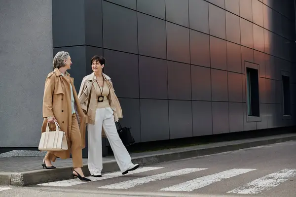 Due donne attraversano con grazia la strada di fronte a un maestoso edificio. — Foto stock
