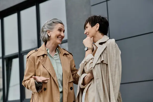 Two professional women, a mature beautiful lesbian couple, walk side by side in front of a modern building. — Stock Photo