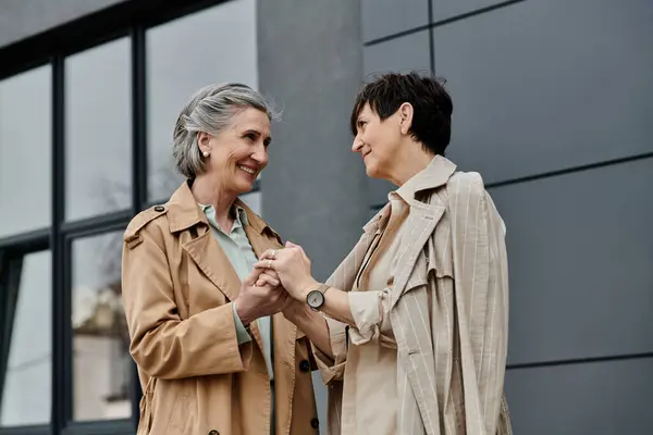 Two women holding hands in front of a modern building. — Stock Photo