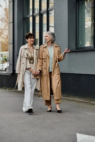 Dos mujeres paseando por la calle de la ciudad mano a mano. - foto de stock