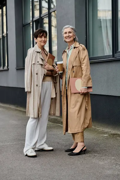 Two elegant women, a mature lesbian couple, stand side by side in front of a majestic building. — Stock Photo