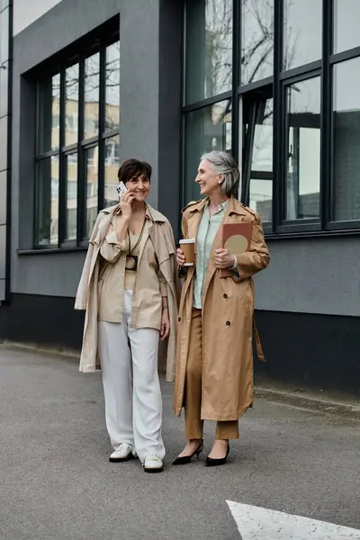 Two mature women, a couple, stand together in front of a building. — Stock Photo