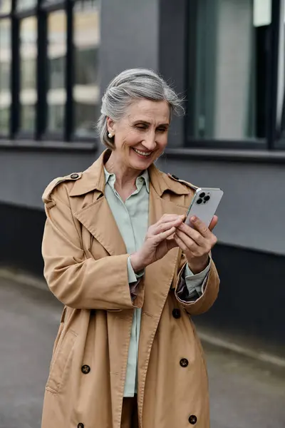 A woman in a trench coat using a cell phone. — Stock Photo