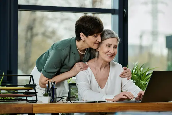 Woman kisses woman on cheek in front of laptop. — Stock Photo