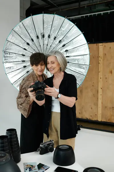 Zwei Frauen stehen zusammen, eine hält eine Kamera in der Hand, die andere lächelt in einem lebendigen Fotostudio-Ambiente. — Stockfoto