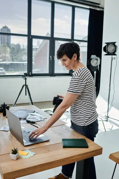 A middle-aged woman stands at a table, engrossed in using a laptop computer. — Stock Photo