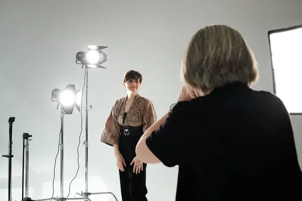 Une femme d'âge moyen se tient en confiance devant une caméra dans un studio lumineux et blanc. — Photo de stock