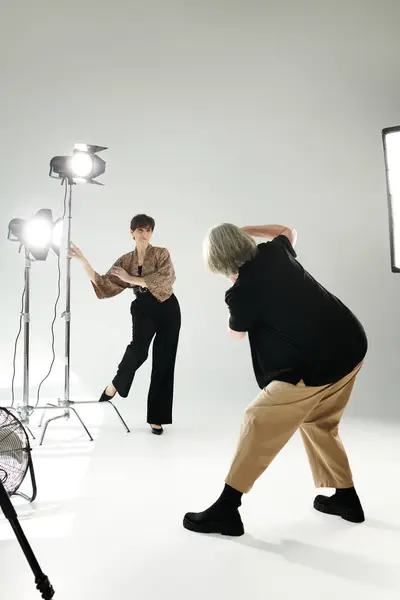 A middle-aged lesbian couple in a bustling photo studio; one expertly capturing moments with a camera, the other striking poses as the model. — Stock Photo