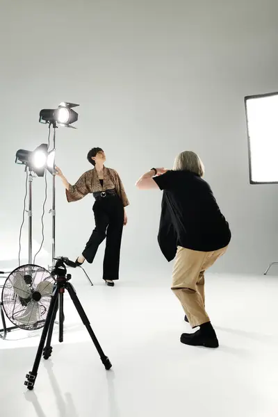 Couple lesbien d'âge moyen dans un studio photo ; une femme tient une caméra, tandis que l'autre pose devant elle. — Photo de stock