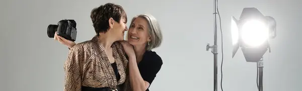 Middle-aged lesbian couple in a photo studio, a woman holds a camera next to a model. — Stock Photo