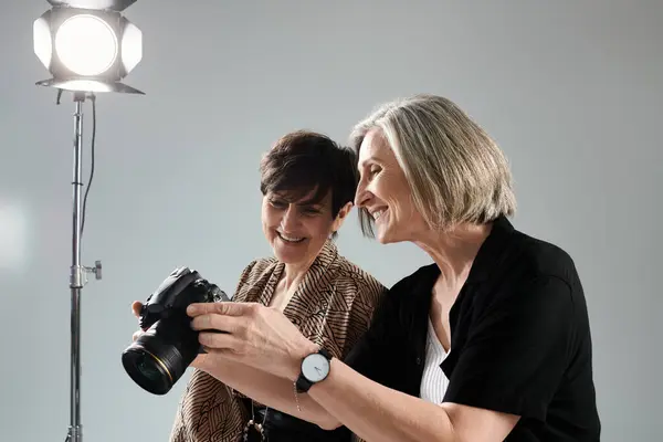 Middle-aged lesbian couple in a photo studio, one with a camera and the other striking a pose. — Stock Photo