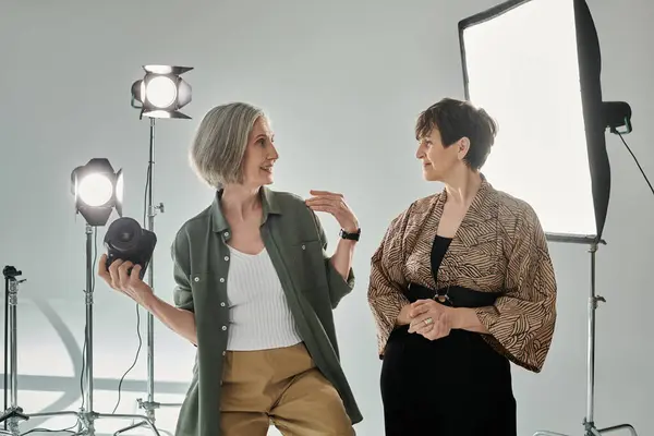 A middle-aged lesbian couple in a photo studio; one woman, a photographer, holds a camera while explaining poses to model. — Stock Photo