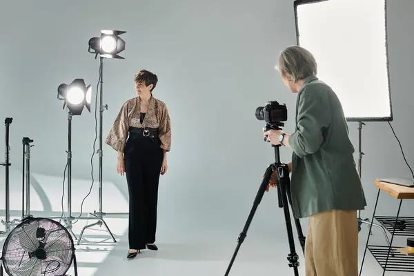 A middle-aged photographer captures her partner as she strikes a pose in a photo studio. — Stock Photo