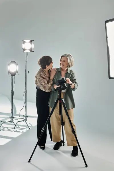 A middle-aged lesbian couple in a photo studio; one behind the camera, the other hugging her — Stock Photo